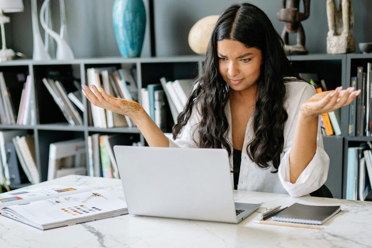 Photo by Yan Krukau: https://www.pexels.com/photo/a-woman-in-white-long-sleeves-using-a-laptop-8837799/ A user holds their hands up in frustration at the computer as their Canva design does not behave as intended