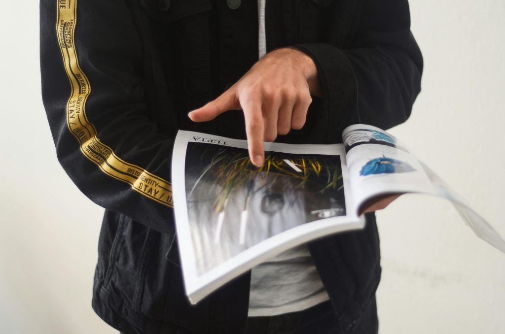 Photo by Gül Işık: https://www.pexels.com/photo/unknown-person-pointing-at-magazine-2385565/ A designer points at a printed page as they indicate this as the final format for their design, so they can keep it in mind while designing
